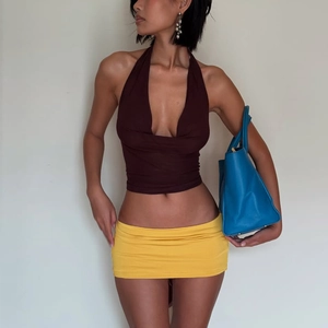 Détail du haut dos nu marron à décolleté plongeant et mini-jupe jaune avec un sac à main bleu