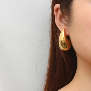 Woman wearing large golden teardrop hollow earrings made of 18K gold-plated stainless steel