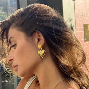 Elegant gold double heart dangle earrings worn by a model in a stylish outdoor setting