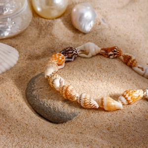 Macro shot of natural cowrie seashell anklet on beach sand with brown speckled textures