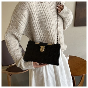 Detail showing woven texture and gold metal buckle on a black rectangular handbag