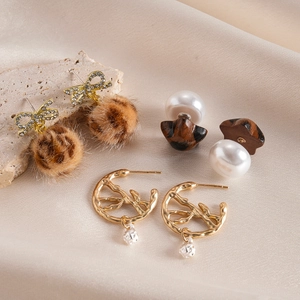 Detailed set of bow leopard fur ball, wood pearl, and gold branch earrings on silk