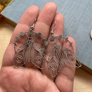 Detail of vintage cicada wing earrings held by hand over dark background books