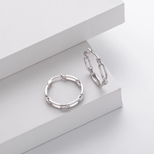 Macro shot of 925 sterling silver chain link hoop earrings on a white geometric pedestal