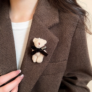 Close-up of a cute beige flocked bear brooch with a velvet bow on a brown herringbone blazer
