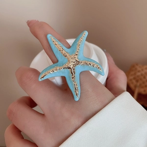 Macro detail of sky blue starfish ring with gold textured center and enamel finish