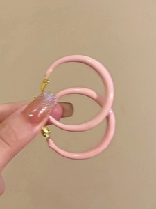 Detailed close-up of pink enamel hoop earrings with golden clasp held by hand