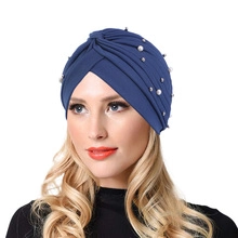 Close-up of blue turban hat featuring shiny pearls and elegant cross-wrap fabric design
