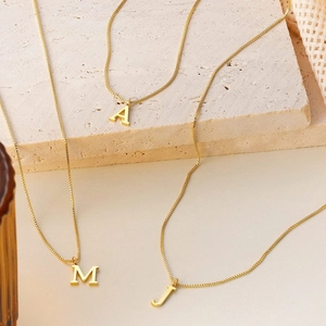 Gold stainless steel initial necklaces A, M, J on box chain presented on stone block