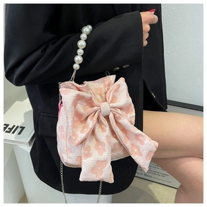 Pink jacquard bow bag featuring a white pearl handle and metal chain on a model