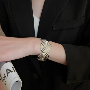 Detail of silver spiral flower bangle with metallic texture worn on a black blazer sleeve