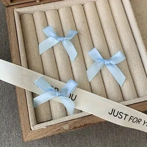 Three sky blue satin bow hair clips displayed in a stylish beige jewelry box