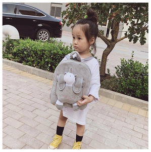 Toddler girl wearing gray plush unicorn backpack with MELF letter print on outdoor street