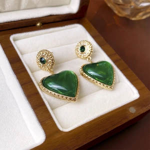 Detail of vintage heart earrings with green gemstone on a premium wooden jewelry box