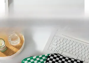Close-up of green and black checkered knit laptop sleeves on a white home desk