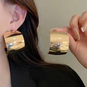 Detail view of large gold wide-hoop earrings featuring a mirror-polished metallic finish