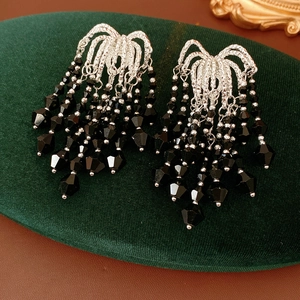 Close-up of elegant silver wavy studs with black faceted glass bead tassels on velvet