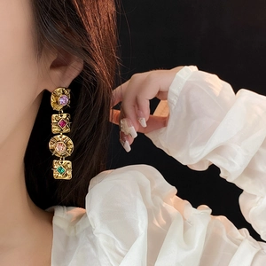Macro detail of vintage gold hammered earrings with colorful gemstones worn by model