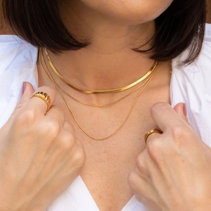 Close-up of layered gold snake chain necklaces and matching rings on a model