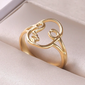 Close-up of golden hollow ring featuring an abstract face design on cream satin