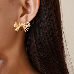 Close-up of golden bow stud earring with brushed metallic texture on a model ear