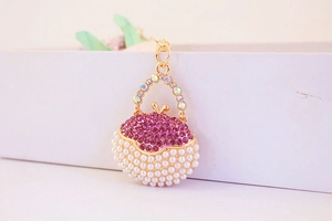 Detail of gold metal handbag charm featuring pink rhinestones and white pearls