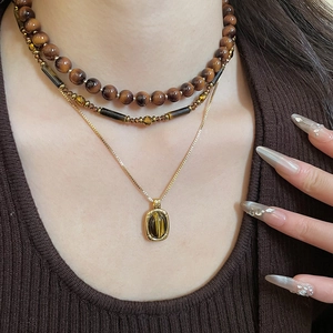 Detail of layered tiger eye pendant necklace set with vintage beads on a brown sweater