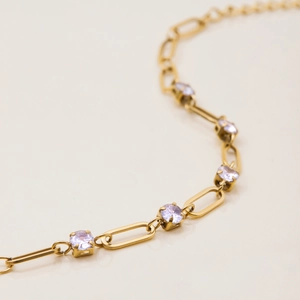 Detailed close-up of gold paperclip chain bracelet with purple zircon and extension chain