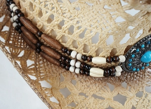 Detail of woven straw cowboy hat featuring ethnic beads and a turquoise metal buckle