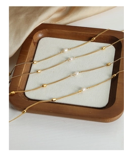 Close-up of four gold plated titanium necklaces with pearls on a wooden display tray