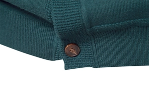 Close-up of dark green knit cardigan featuring ribbed hem and tortoiseshell button detail