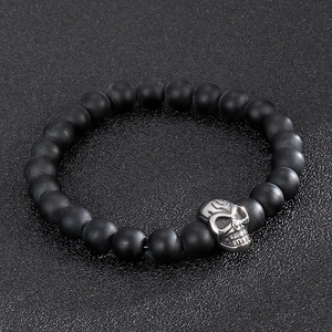 Detail of 8mm matte black beaded bracelet featuring a silver skull charm on a dark surface
