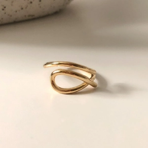 Detail of a gold-plated twisted minimalist ring showing polished curves on white surface