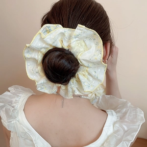 Close-up of light yellow floral fabric scrunchie with lace trim on model hair
