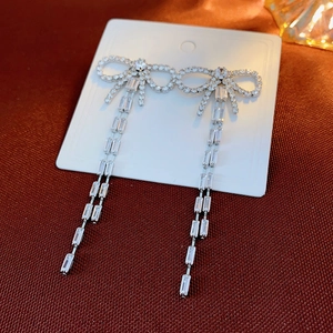 Detailed view of silver bow drop earrings with sparkling rhinestone tassels on display