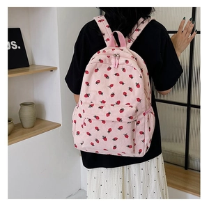 Pink corduroy backpack with red strawberry prints worn by a model in a cozy home setting