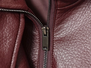 Detail of silver metal zipper and textured faux leather fabric on burgundy jacket