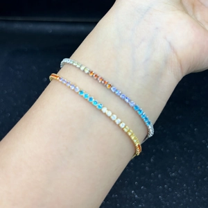 Detail shot of gold and silver rainbow zircon bracelets worn on a wrist over dark background