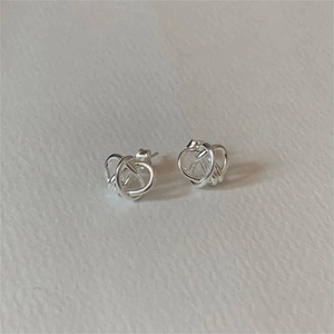 Close-up of silver knot stud earrings in a minimalist woven design on a textured background