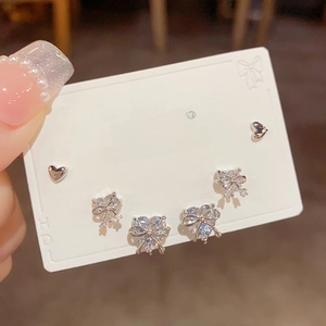 Detailed close-up of a silver earring set with heart and bow designs and zircon stones