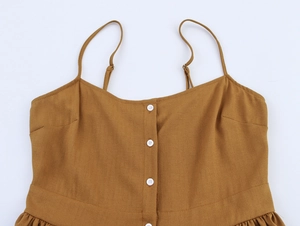 Détail de robe d'été caramel avec boutons blancs et fines bretelles sur tissu en coton