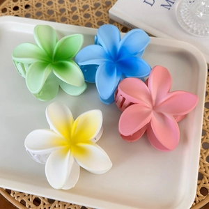 Detailed close-up of matte frangipani flower hair claws in pastel summer colors