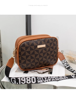 Detail of a brown geometric crossbody camera bag on a glass table with a wide strap