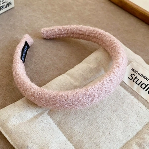 Close-up of pink plush teddy fabric headband with black handmade label on canvas background