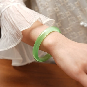 Close-up of a light green cat's eye stone bangle with silky luster on a model's wrist