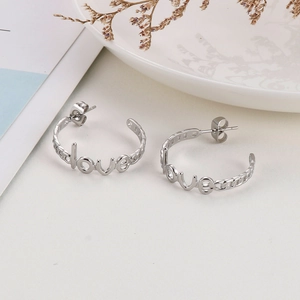 Detail view of silver C-shaped Love earrings featuring hollow lettering on a white ceramic plate