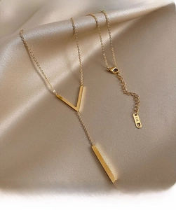 Close-up of golden V-shaped titanium necklace with K18 engraving detail on silk background