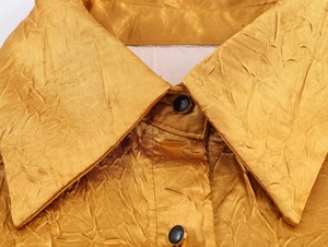 Detailopname van gouden satijnen jurkkraag met geplooide textuur en zwart-gouden knoop