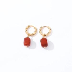 Detailed shot of golden hoop earrings with red geometric natural stone pendants