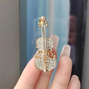 Detail view of a gold violin brooch with sparkling rhinestones held by fingers